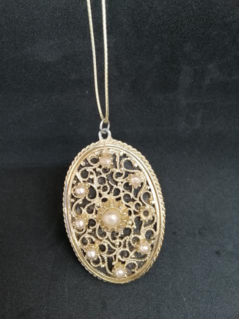 Collier en métal doré avec pendentif avec de perles et derrière un miroir